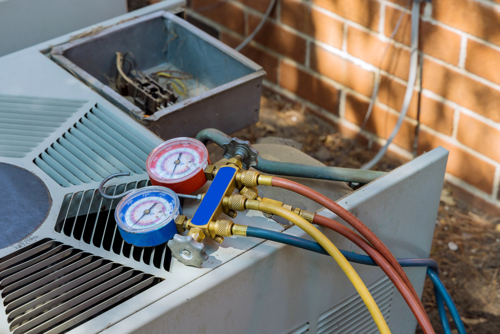 HVAC manifold gauge set connected to the service ports of an outdoor air conditioning unit during a maintenance or repair session.