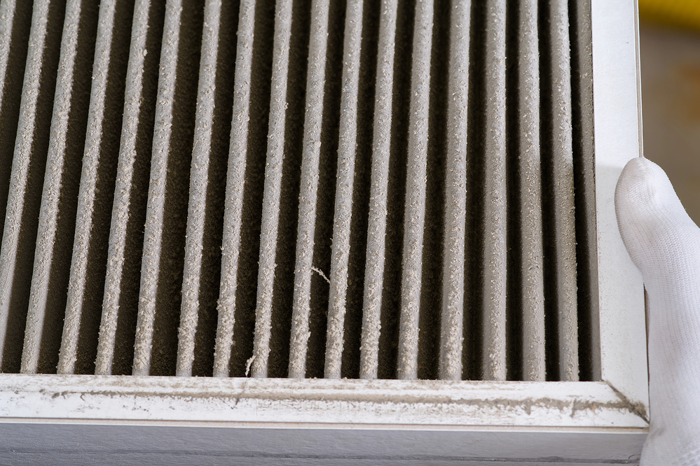 A close-up of a hand holding a dirty air filter with visible dust and debris buildup between the pleats.